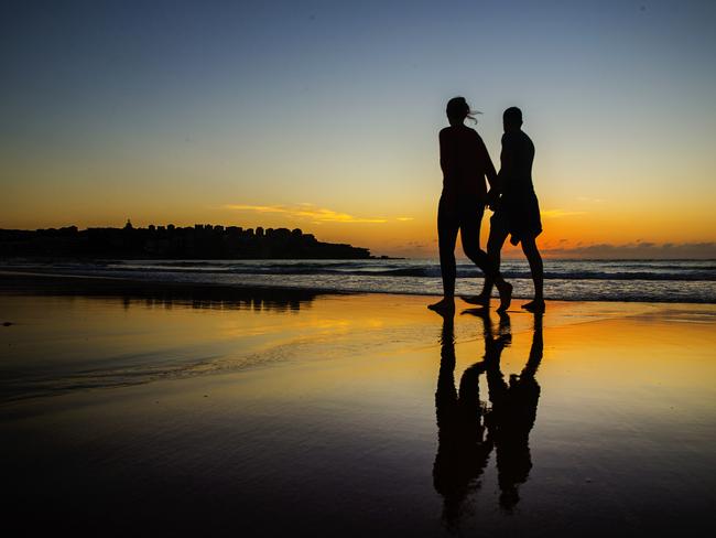 A couple take a beach walk at Bondi at dawn. Picture: Jenny Evans