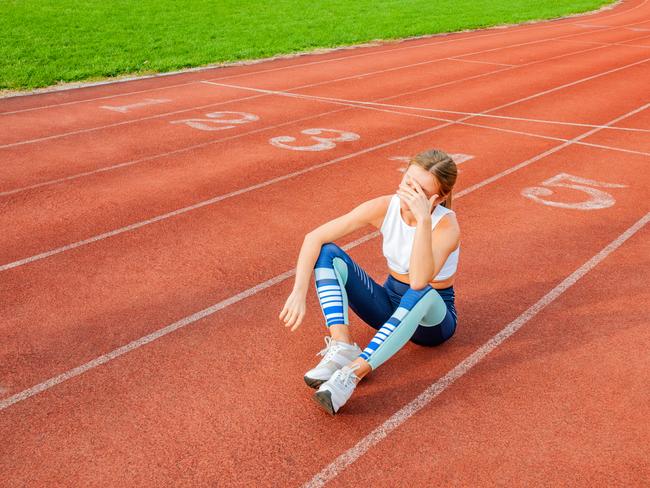 Tired woman runner taking a rest after run sitting on the running track