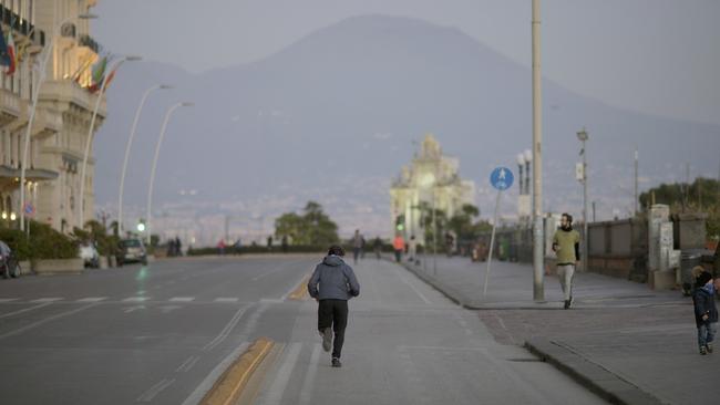 A man jogs along an empty Naples street with Mt Vesuvius in the background. Picture: AP