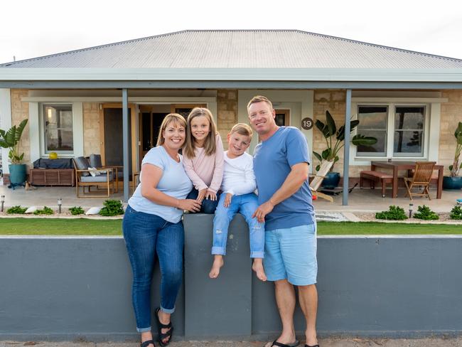 Outdoors portrait of a happy family of four smiling in front of new dream home or vacation rental house. Mom, dad, and children boy and girl, embracing and having fun together enjoying holiday villa.