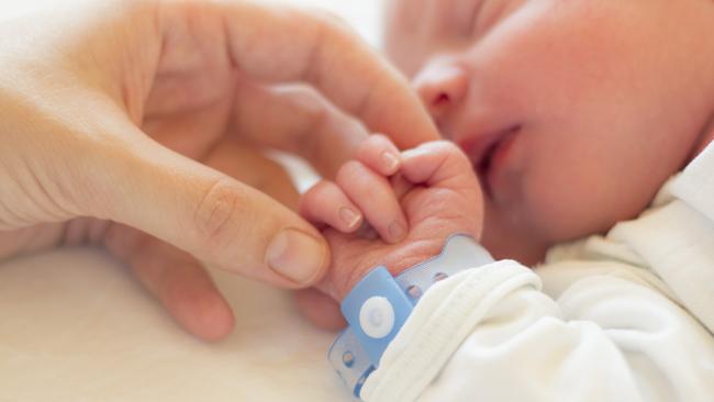 Newborn baby boy sleeping in his crib, his mother's hand holding his little hand.