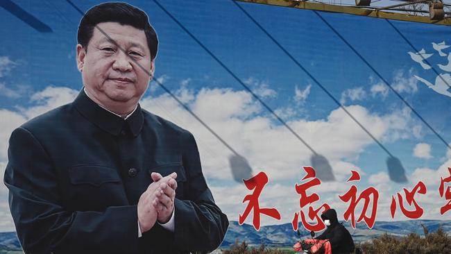 A man rides a scooter past a billboard showing Chinese President Xi Jinping with a slogan which reads 