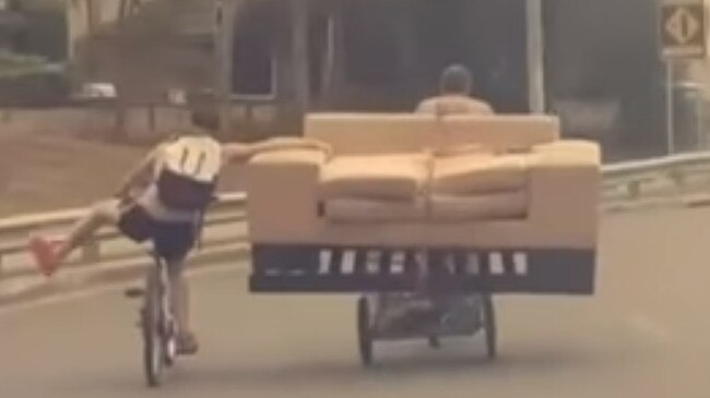 Two men ride through a roundabout with a couch on the back of a pushbike in Macquarie Fields.