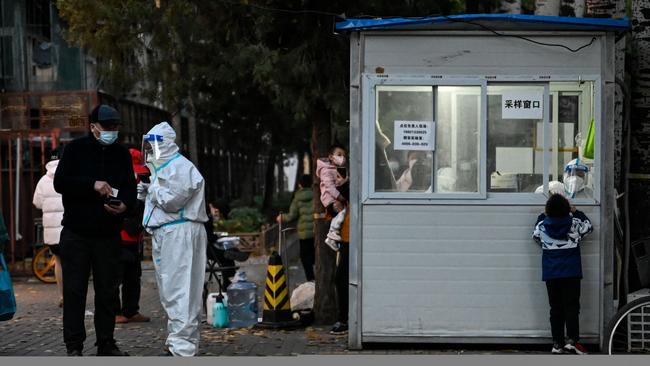 A health worker talks with a man while a health worker inside a nucleic acid testing station gets a swab sample from a boy to be tested for Covid-19 coronavirus in Beijing. Picture: AFP