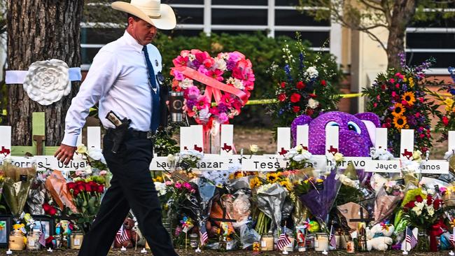 A police officer walks past a makeshift memorial for the shooting victims outside Robb Elementary School in Uvalde, Texas. (Photo by CHANDAN KHANNA / AFP)