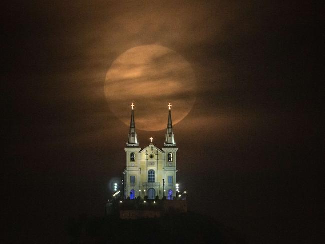 The full moon descends behind the Nossa Senhora da Penha Church in Rio de Janeiro, Brazil. Picture: Yasuyoshi CHhiba