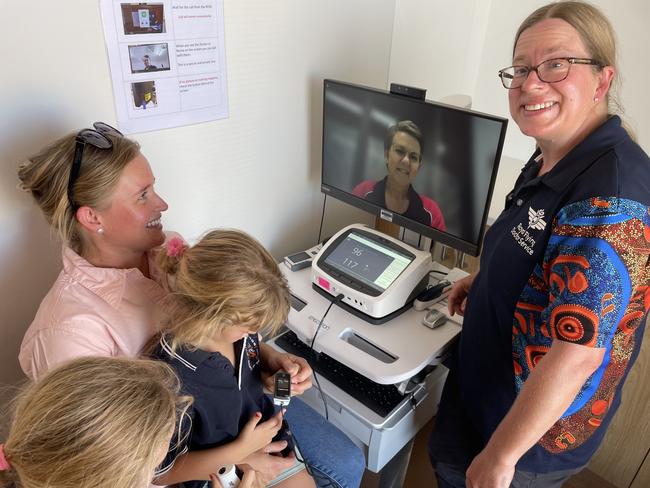 Outback cattle station resident Chantelle Williams with her children Bonnie, 5, and Olivia (obscured) 6 use the new telehealth emergency facility to speak with Royal Flying Doctor Service digital health projects officer Michelle Dobie in Adelaide, watched by RFDS primary care clinical director Dr Amanda Bethell in William Creek, South Australia. Picture: Mark Day