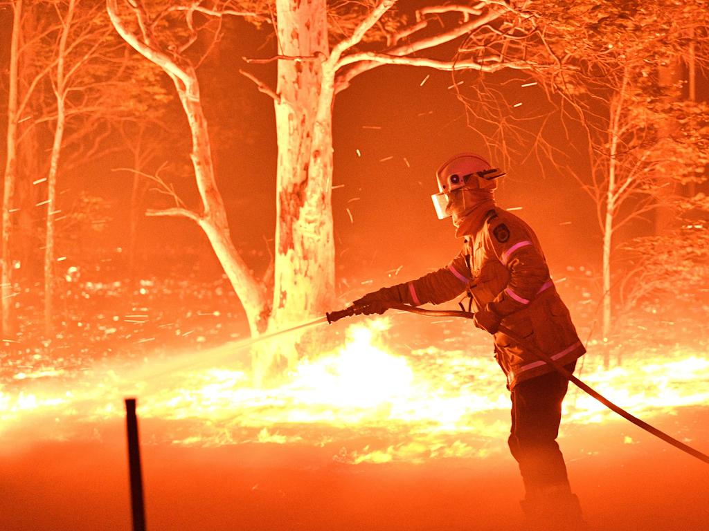 A firefighter hosing down trees and flying embers in an effort to secure nearby houses from bushfires near the town of Nowra. Picture:AFP