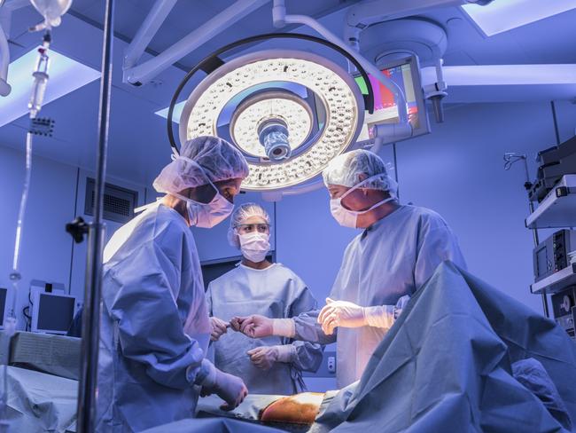 Doctors wearing surgical masks and gowns performing an operation on patient in hospital operating theater.