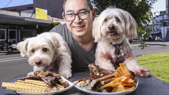 Anthony Wallace with Daisey and Baileys try out the dog menu, which includes Peking duck jerky and kangaroo ribs. Picture: Wayne Taylor