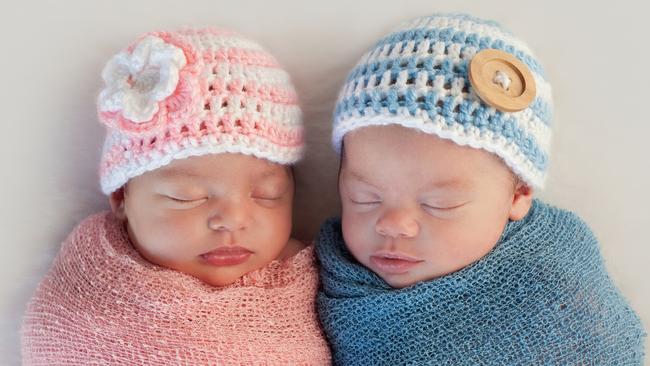 Five week old sleeping boy and girl fraternal twin newborn babies. They are wearing crocheted pink and blue striped hats.