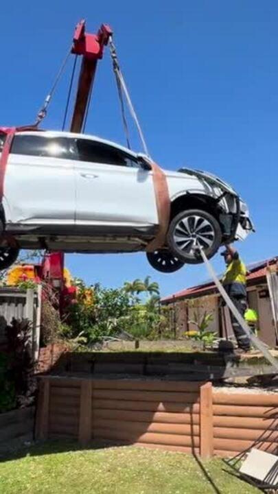 A crashed car is removed by crane from a garden