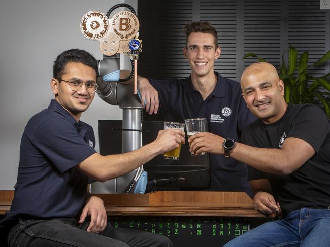 ADELAIDE, AUSTRALIA - Advertiser Photos DECEMBER 15, 2021: Computer Scientists/ Bar-Tender Robot and Beer recipe Designers Josh Vira (left) and Christopher Fusco (back) pour a beer for Barossa Valley Brewing collaborator Denham D'Silva (right) at the Australian institute of Machine Learning at Lot Fourteen, SA. Picture: Emma Brasier