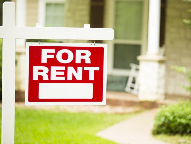 Red and white "House for Rent" sign in front of a stone, wood house that is a rental property. Green grass and bushes indicate the spring or summer season. Front porch and windows in background. Real estate sign in residential neighborhood.  Moving house, relocation concepts.