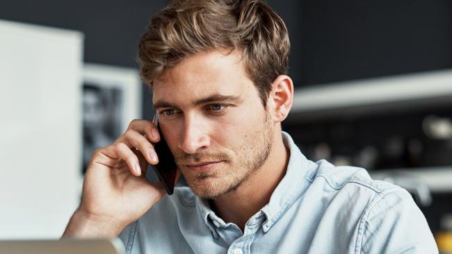 Shot of a young man talking on his cellphone while using his laptop at home