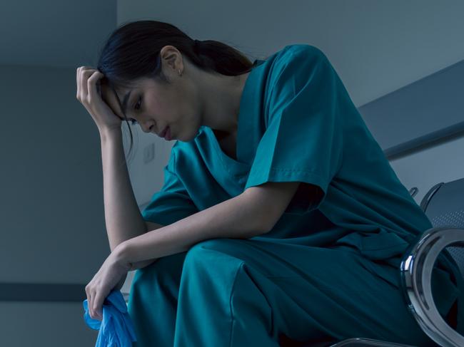 Medical nurse is sitting down a the hospital corridor in frustration and grief after failure and patient body condition