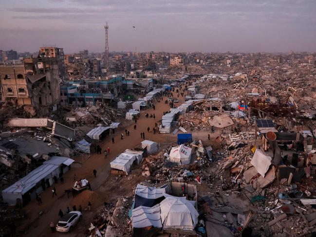 TOPSHOT - Palestinians walk past tents lining the streets amid the rubble of destroyed buildings in Jabalia, in the northern Gaza Strip on February 18, 2025, as people return to northern parts of Gaza during a current ceasefire deal in the war between Israel and Hamas. Israeli Prime Minister Benjamin Netanyahu said on February 17, that he was "committed" to US President Donald Trump's plan for Gaza, which involves displacing more than two million inhabitants of the Palestinian territory. (Photo by Omar AL-QATTAA / AFP)