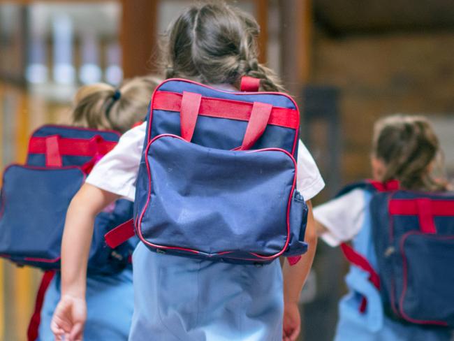 Rear view of excited students running towards entrance. Girls are carrying backpacks while leaving from school. Happy friends are wearing school uniforms. Source: iStock