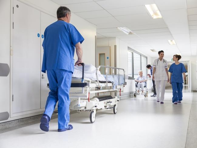 Male nurse pushing stretcher gurney bed in hospital corridor with doctors & senior female patient