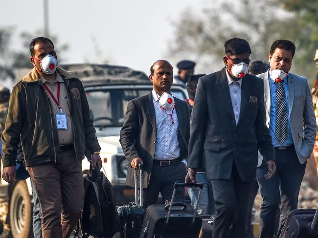 Indian nationals evacuated from the Chinese city of Wuhan, following government's decisions against the coronavirus outbreak, wear protective facemasks as they carry their belongings on a road at Indira Gandhi International Airport in New Delhi on February 1, 2020. - The foreign ministry said January 29 it has now requested permission to operate two flights to remove nationals from China, and that the Indian embassy in Beijing was in talks with local authorities. (Photo by Money SHARMA / AFP)