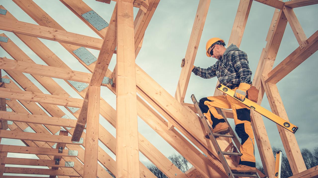 Caucasian Wood Skeleton Frame Worker on Top of New Constructed House Structure Staying on Ladder with Spirit Level.