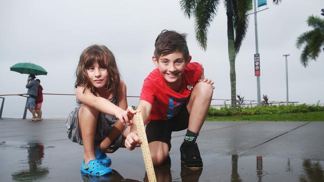 On Monday Cairns Airport Alert beat its record 24 hour rainfall total for April. Abby Vita, 7, and her cousin Tom Dobby, 11, measure the total on a ruler while on a wet walk along the Esplanade. Picture: Brendan Radke