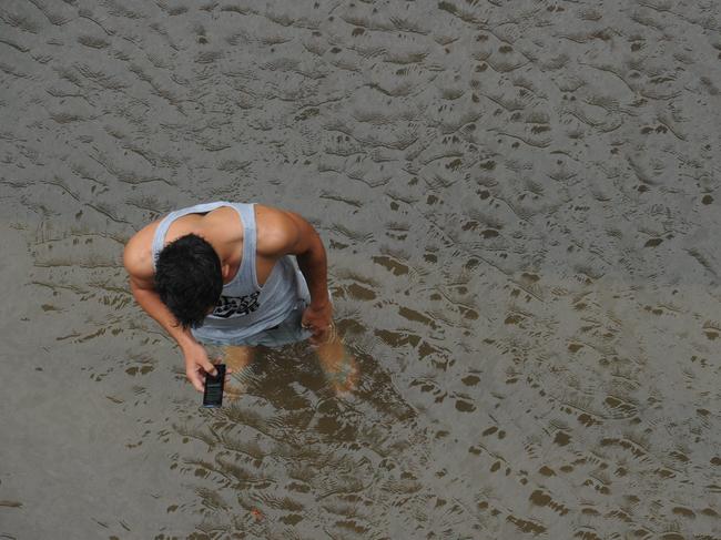 Aftermath from Cyclone Yasi in Townsville. Residents wade A local resident in Townsville make a mobile call in flooded waters.