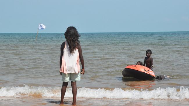 Kids play in the water at Blue Mud Bay, where a sea rights flag can be seen waving at the intertidal mark Picture: Matt Garrick