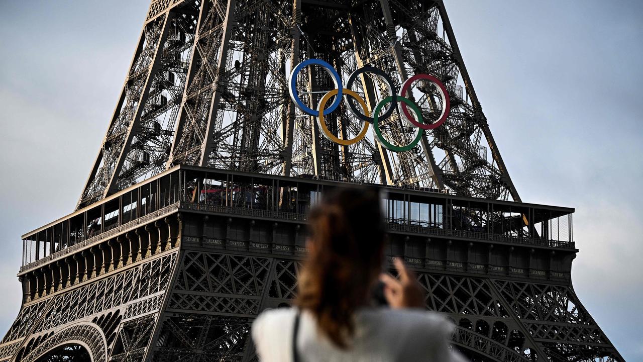 A woman takes a picture of the Eiffel Tower decorated with the Olympic rings ahead of the Paris 2024 Olympic Games. Picture: Julien de Rosa / AFP