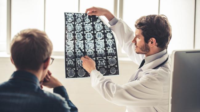 Gold Coast Suns - My Life - Tasman Oncology Research.Handsome young doctor in white coat is showing x-ray image to his patient while working in office