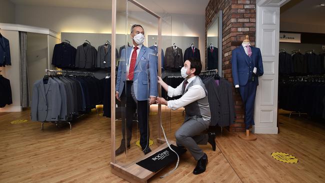 Tailor Gary Keenan, right, of Bogart Menswear in Belfast, Northern Ireland, measures up a suit using a customer pod designed to keep customers safe from COVID-19. Picture: Getty Images