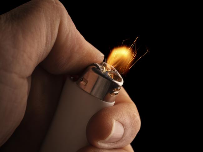 Hand lightning a lighter with a flame freezed in motion on a black background.