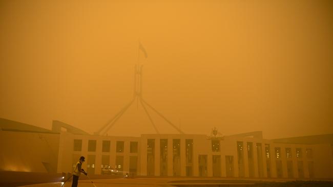 A man cleans the forecourt of Parliament House surrounded by smoke haze early morning in Canberra. (AAP Image/Lukas Coch)