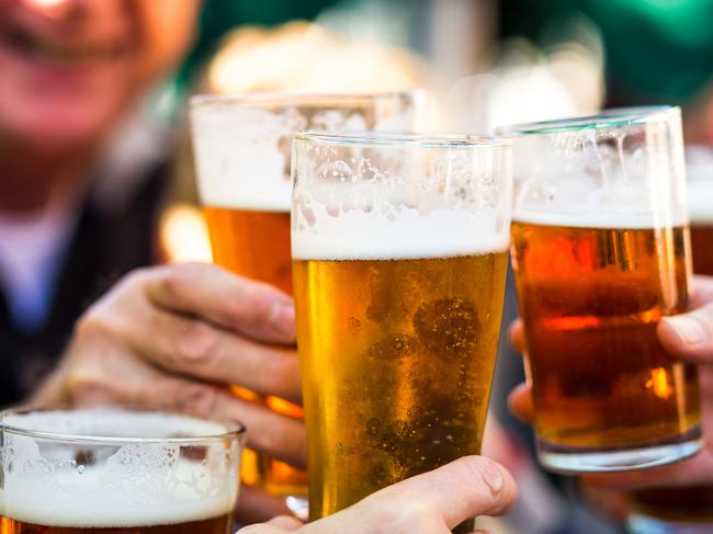 Close up color image depicting a group of people celebrating with a toast. The people cheers their glasses of beer (pints of beer) together in a gesture of celebration, togetherness and happiness. The people are defocused in the background, while focus is on the glasses of beer in the foreground. Room for copy space.