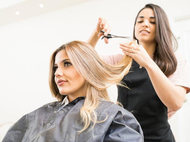 Pretty brunette working as a hairdresser and cutting hair tips of a female customer in a beauty salon