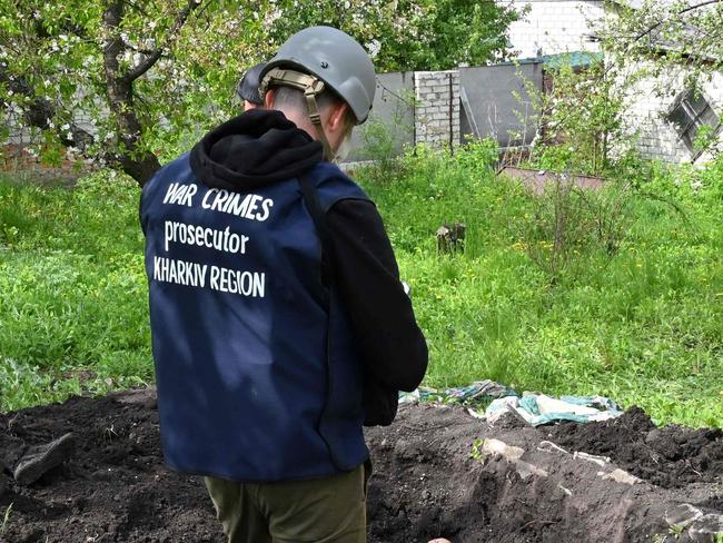 An investigator stands by bodies exhumed from a grave in Stepanky, near Kharkiv. Picture: Sergey Bobok/AFP