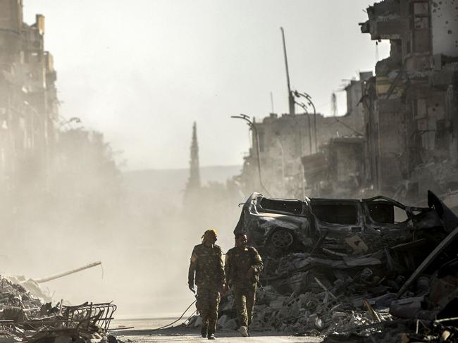 (FILES) This file photo taken on October 20, 2017 shows fighters of the Syrian Democratic Forces (SDF) walking down a street in Raqa past destroyed vehicles and heavily damaged buildings after a Kurdish-led force expelled Islamic State (IS) group fighters from the northern Syrian city, formerly their "capital". 2017 will be remembered as the year the Islamic State organisation's ultra-violent experiment in statehood was terminated but Iraq and Syria are left staring at ruined cities and daunting challenges. / AFP PHOTO / BULENT KILIC