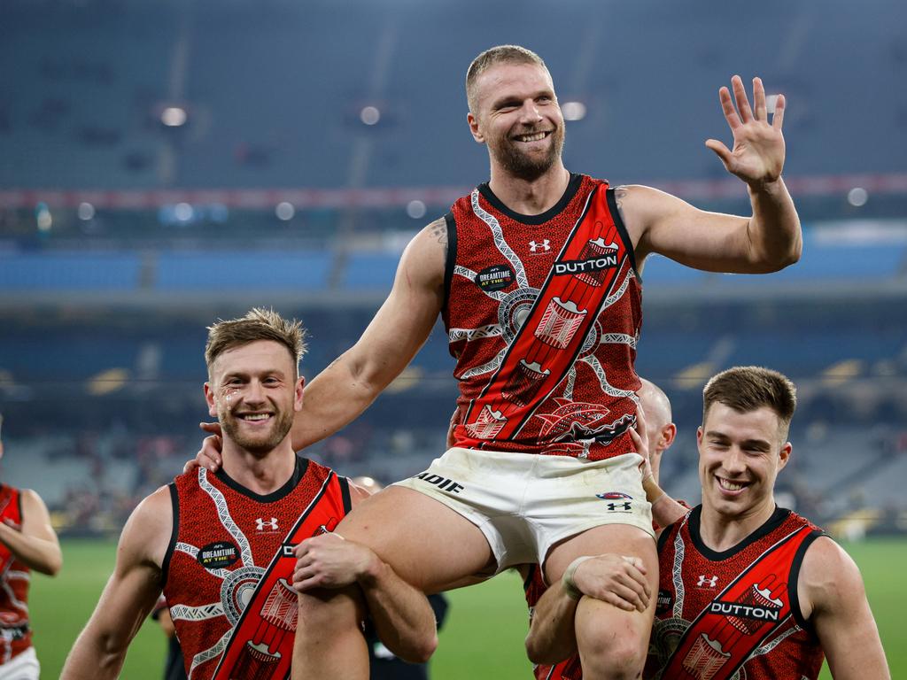 Jake Stringer of the Bombers is chaired off the ground by Jayden Laverde and Zach Merrett, with Nick Hind visible in the background. Picture: Dylan Burns/AFL Photos via Getty Images.