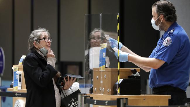 A traveller pulls down her protective mask as a TSA agent compares her face to her identification at a security entrance at Seattle-Tacoma International Airport on Washington. All airlines operating at the airport require employees and passengers to wear face coverings. Picture: Elaine Thompson/AP