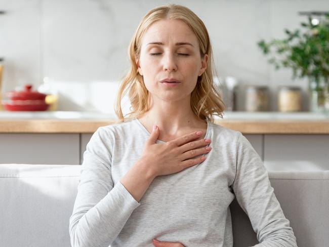 Concept of mental health. Woman sitting on couch and doing calming breathing exercises after panic attack. Female inhaling and exhaling to deep breath. Self-control, anxiety relief concept