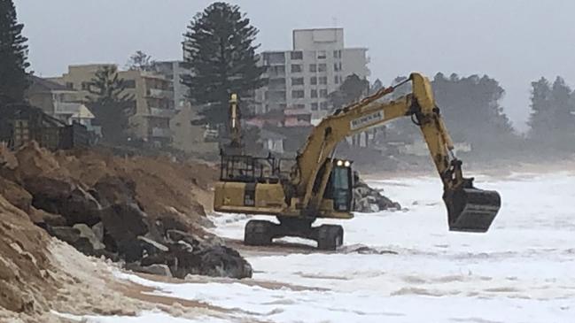 An excavator working to reinforce a temporary sand berm in front of homes on Collaroy/South Narrabeen Beach where part of a permanent sea wall is being built. Picture: Jim O'Rourke