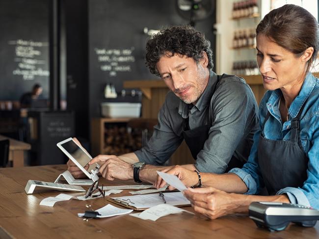 Man and woman sitting in cafeteria discussing finance for the month. Stressed couple looking at bills sitting in restaurant wearing uniform apron. CafÃ© staff sitting together looking at expenses and bills.