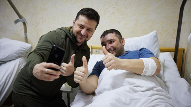 Ukrainian President Volodymyr Zelensky, left, snaps a selfie with an injured man during a visit at a military hospital following fighting in the Kyiv region. Picture: AFP