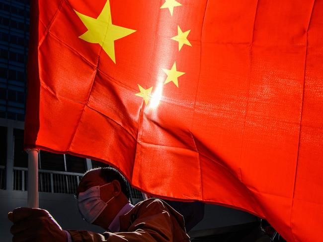 A pro-Beijing supporter holds China's national flag as he and others gather outside the Legislative Council in Hong Kong on November 12, 2020, a day after the city's pro-Beijing authorities ousted four pro-democracy lawmakers. (Photo by Anthony WALLACE / AFP)