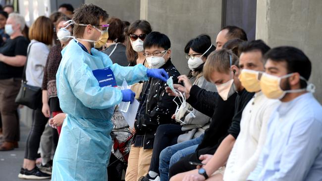 A health care worker hands out face masks to people waiting to be be tested for the coronavirus outside Royal Melbourne Hospital. Picture: Andrew Henshaw