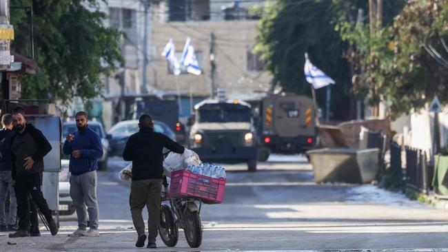 A Palestinian pushes his bicycle loaded with supplies as Israeli forces in armoured vehicles conduct a raid in Jenin. Picture: AFP