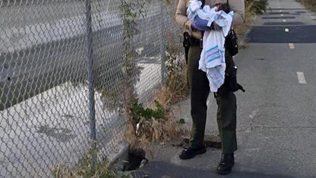A policeman holds the baby beside the hole where she was found.