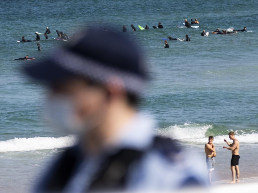 People surf at Bondi Beach as police patrol.