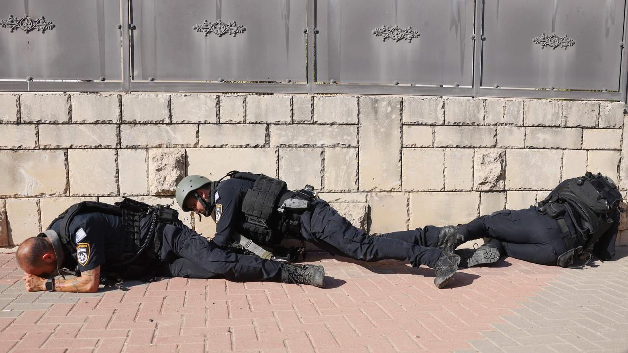 Members of the Israeli forces take cover on the side of a street in Ashkelon as sirens wail while barrages of rockets are fired from the Gaza Strip. Picture: AFP