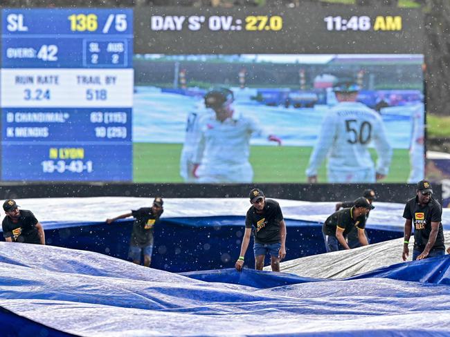 Groundsmen cover the field as rain halts play. Picture: AFP